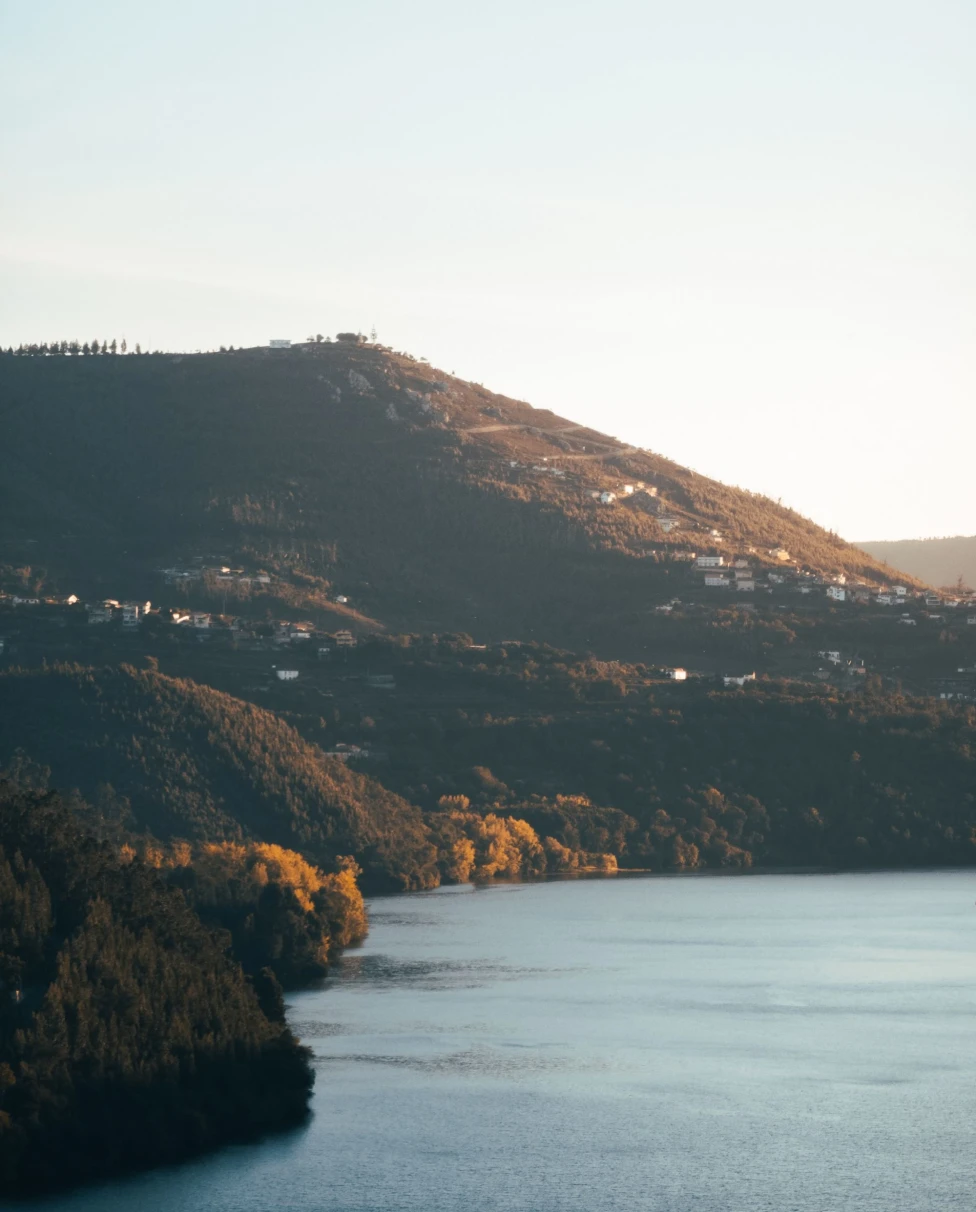a shadowed lush hillside spotted with houses at sun set on a wide river
