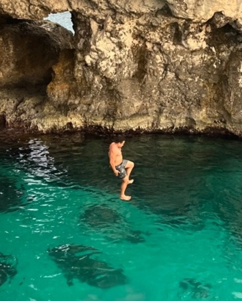 A man jumping from a cliff into clear water.