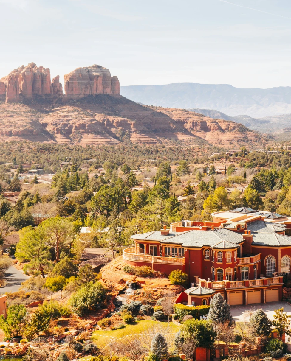 A view of red rock canyons, desert terrain and an elaborate red and orange toned building in the forefront.