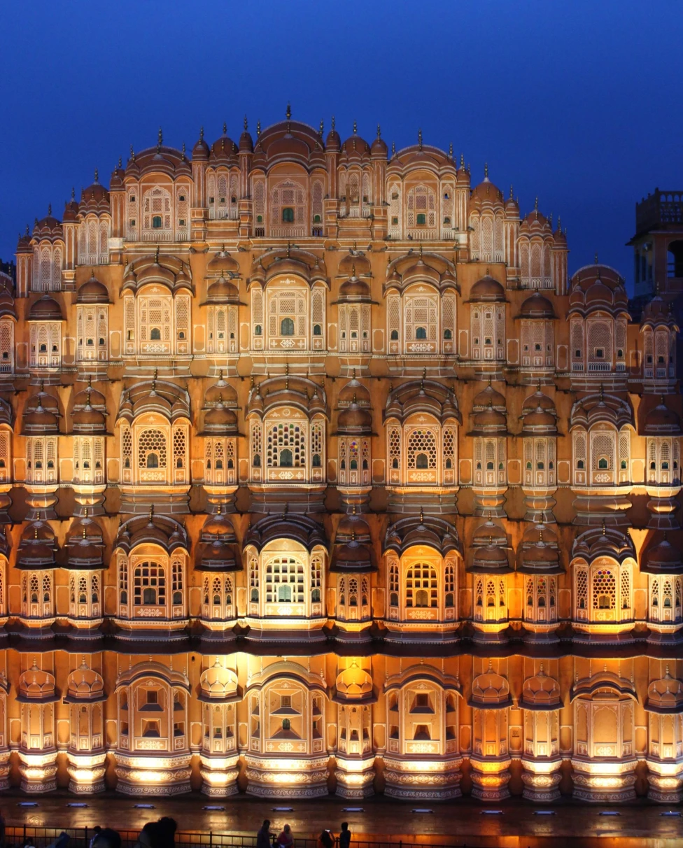 a tiered building lit up at night with a bright blue sky at night above
