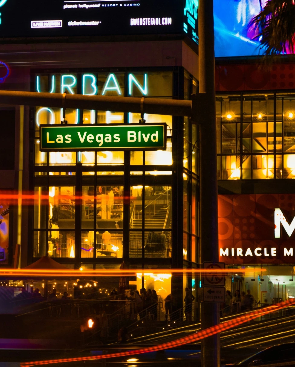 Street sign that reads "Las Vegas Blvd on a street with buildings and neon signs at night.