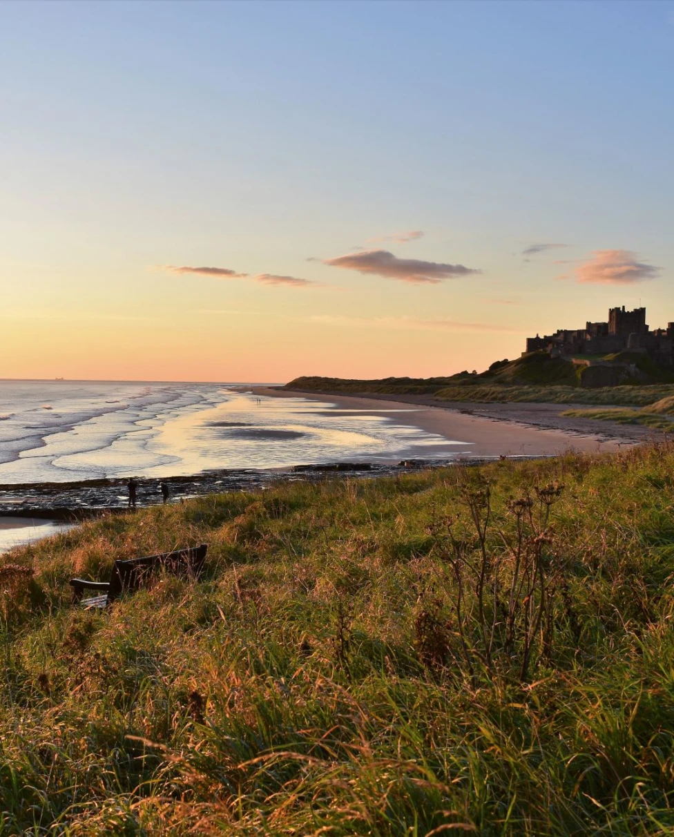 A beach with green field and a castle at the back.