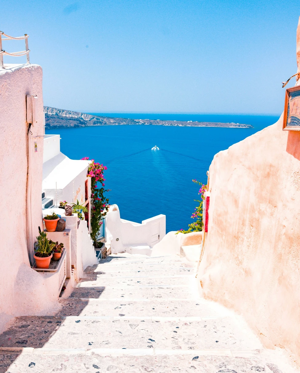 Pink stairs going down with view of ocean with a boat.