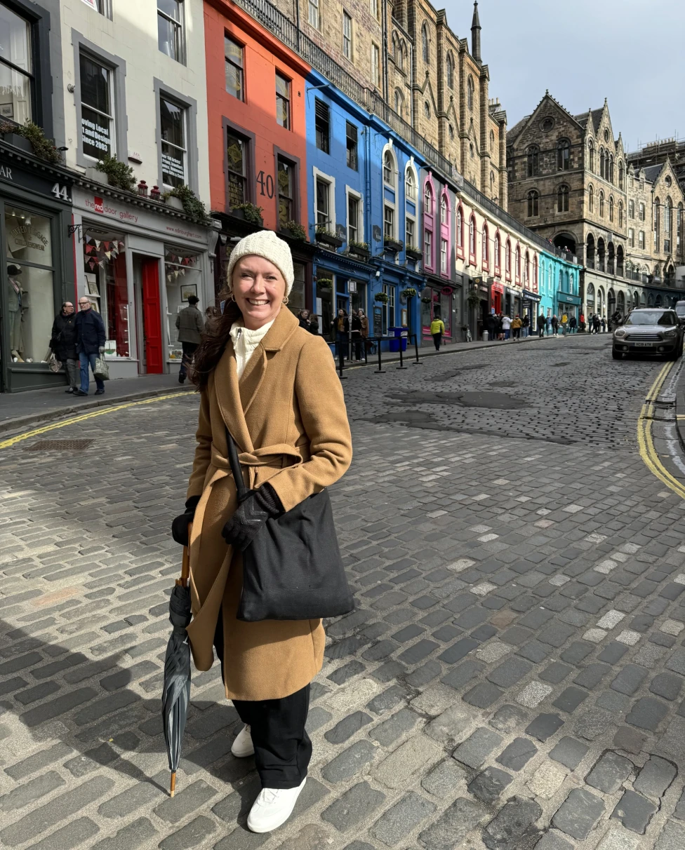 A vibrant urban scene with an Advisor on a cobblestone street during her route from Edinburgh to Glasgow, set against a backdrop of colorful buildings.