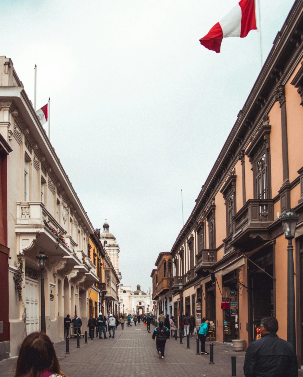 People on street between white and brown buildings.