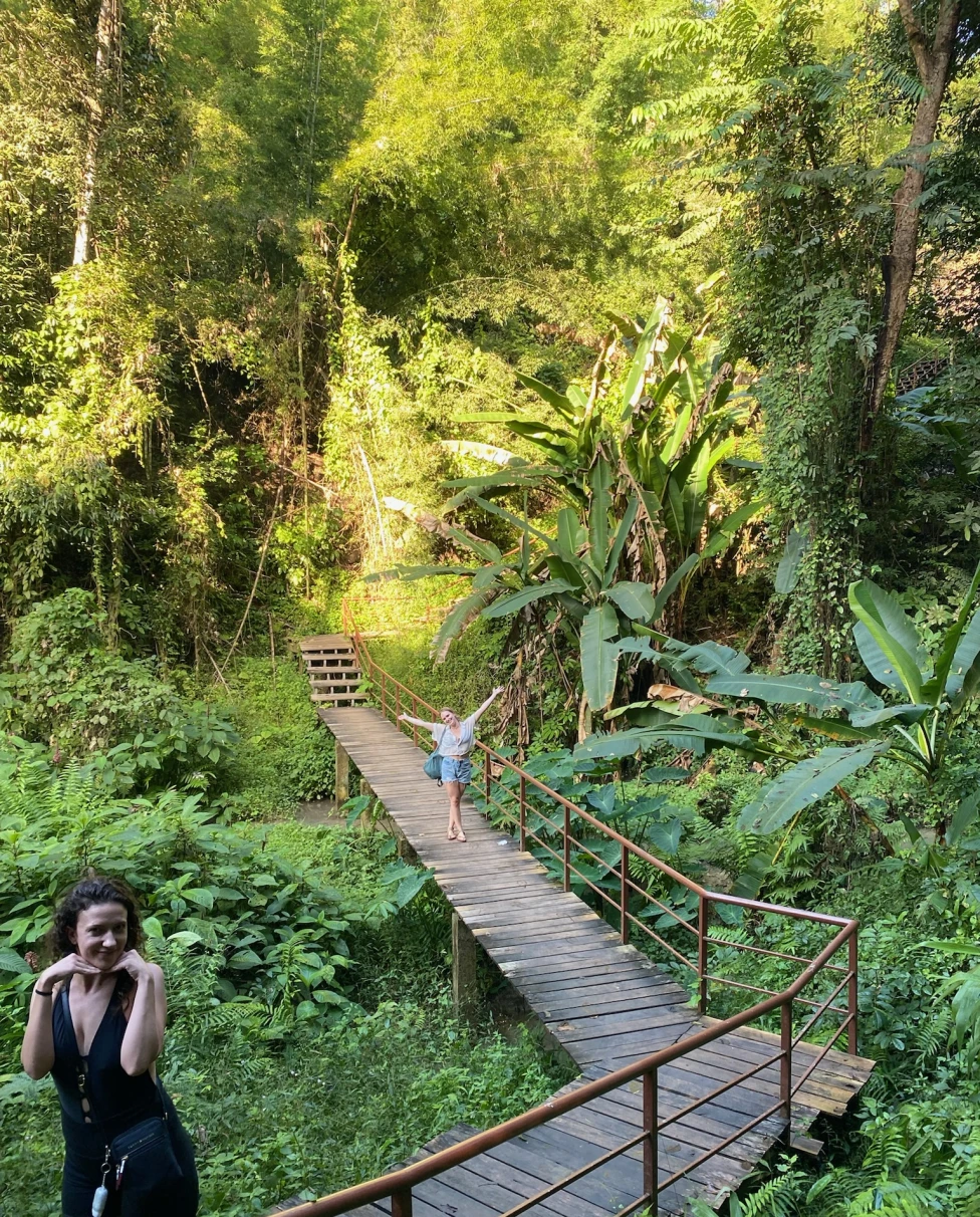 Two women posing on a path surrounded by lush and green plants and trees.