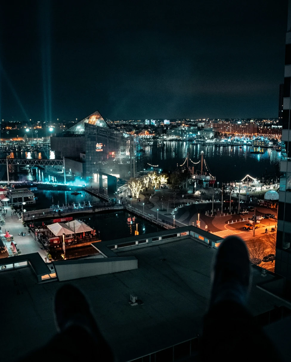 A nighttime cityscape with illuminated buildings and a waterfront, viewed from a high vantage point.