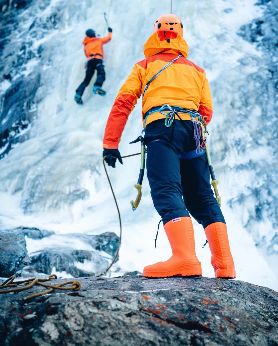 Two people ascending an icy mountain, with ropes, gear and orange outfits.