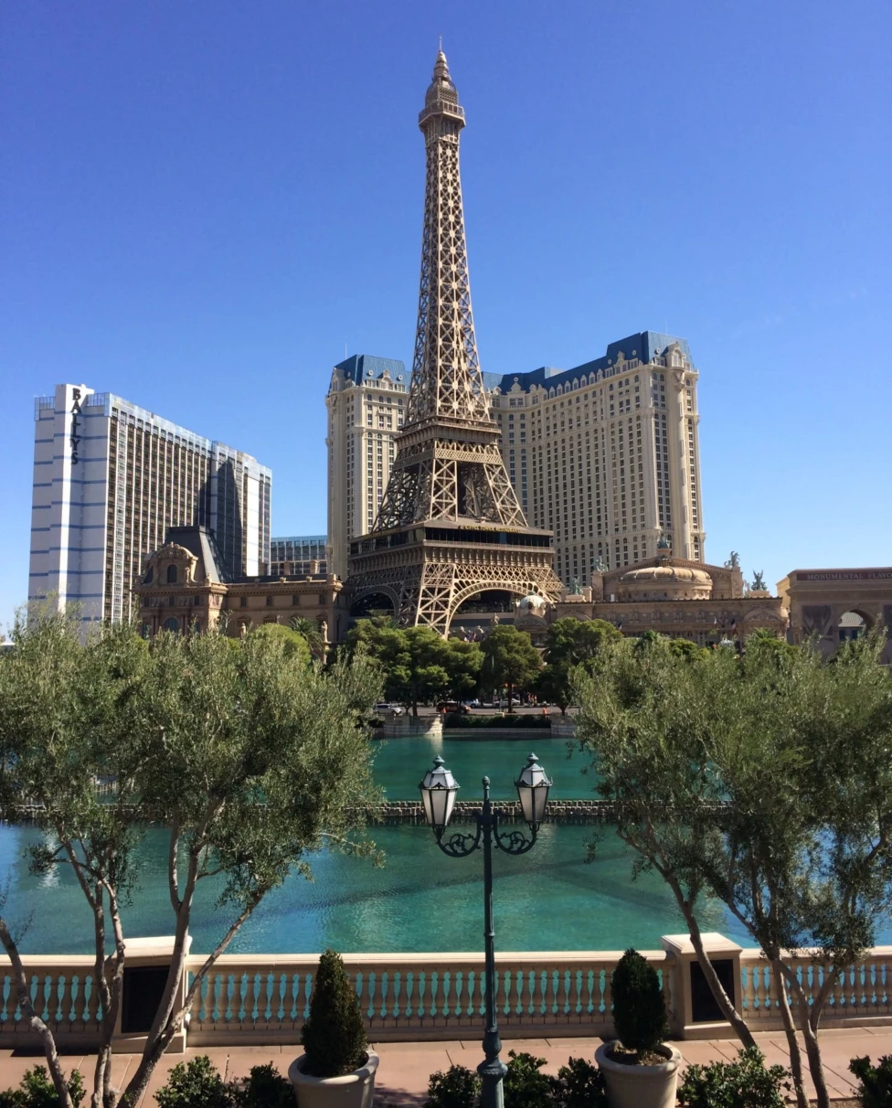 A picturesque replica of the Eiffel Tower by a calm body of water, flanked by greenery and Parisian-themed architecture.