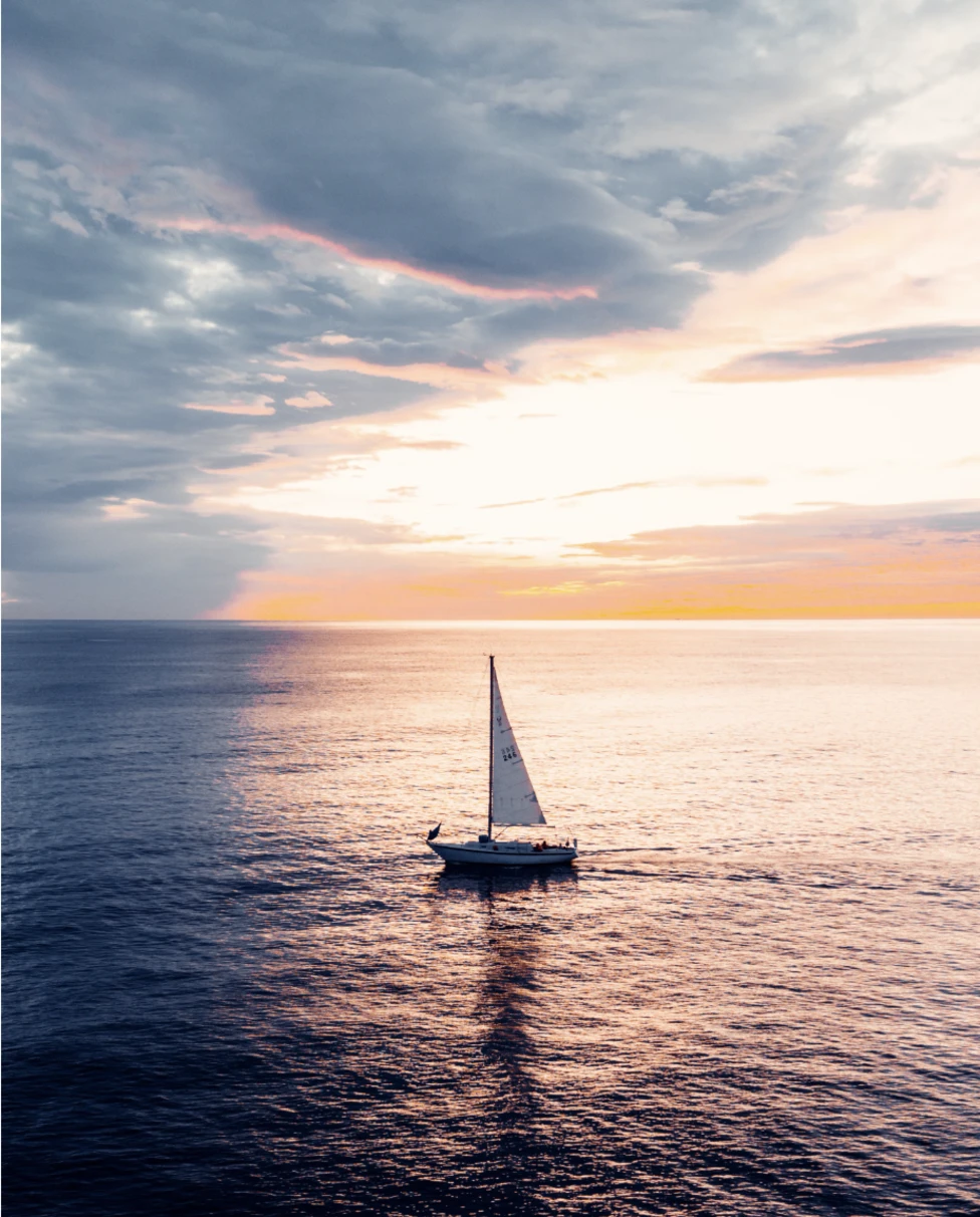 A view of a sailboat at sunset over the water.