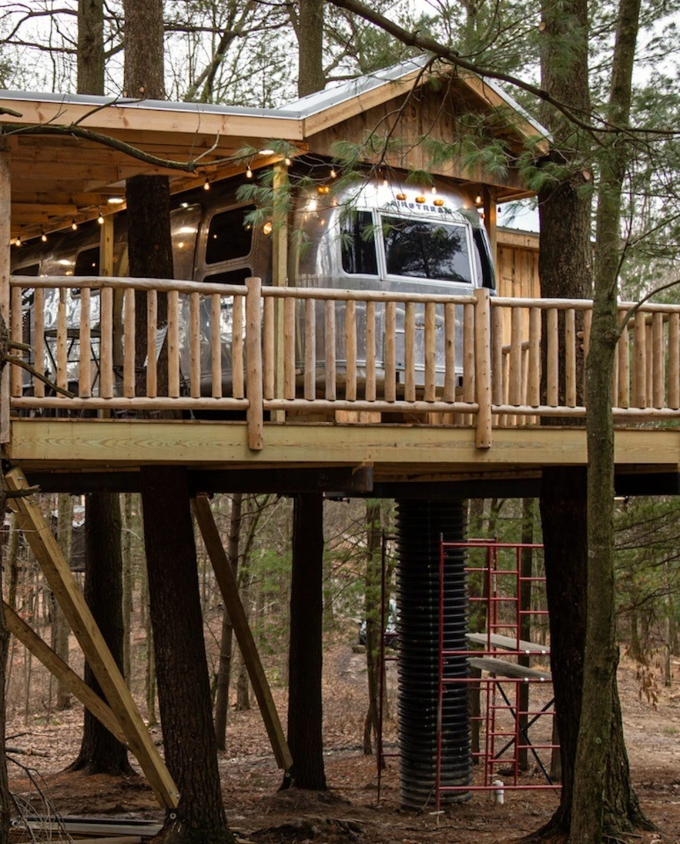 A treehouse in a forest with RV parked in it.