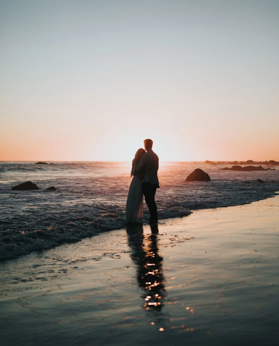 A couple standing near the beach during sunset.