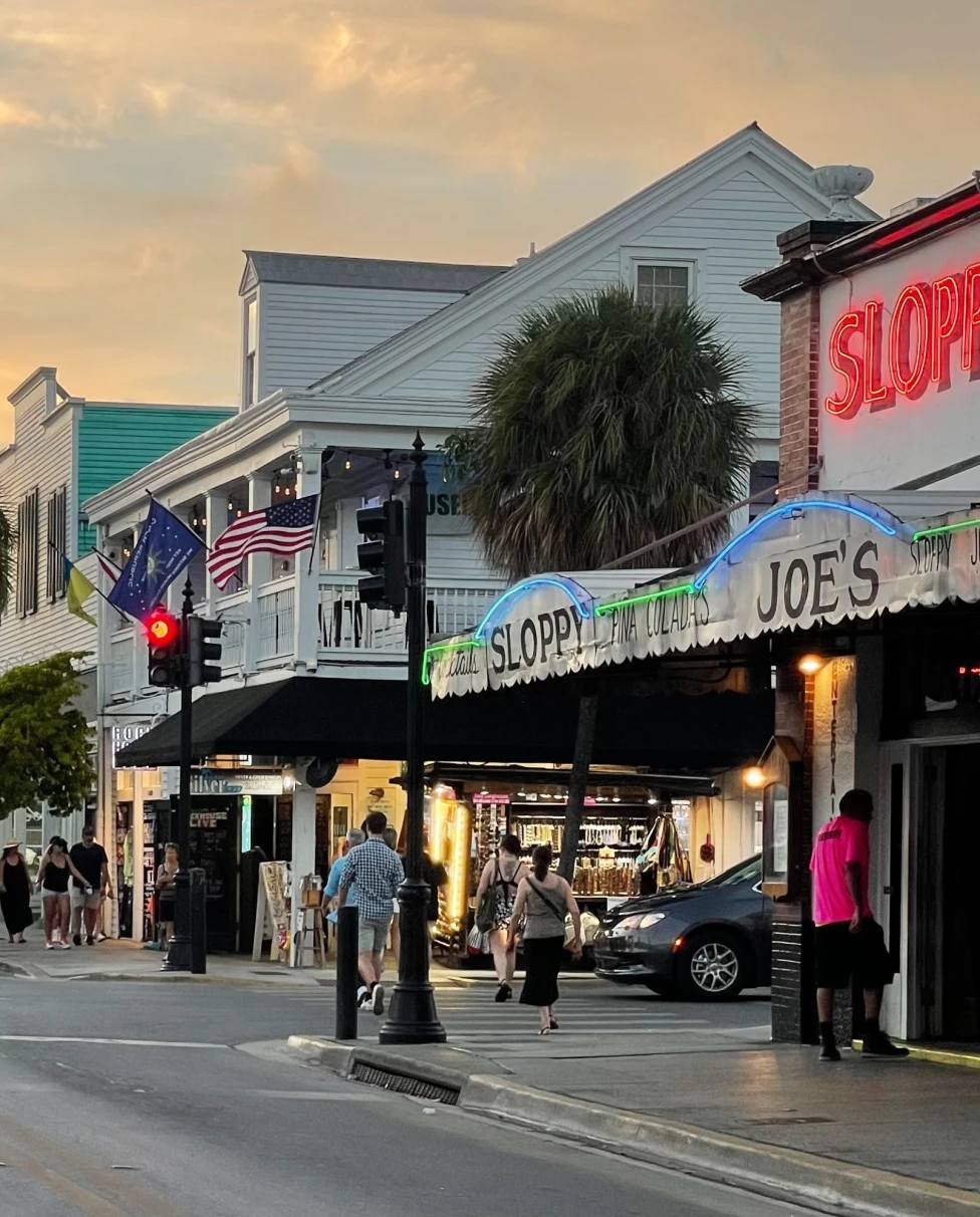 A bustling street scene at dusk with neon signs, American flags and pedestrians.