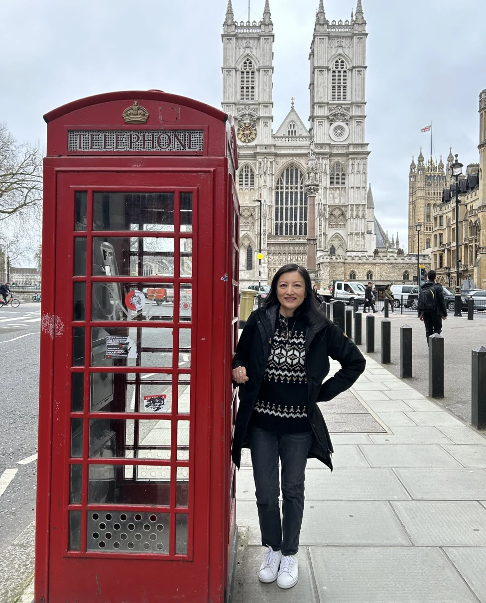 An image of a woman posing next to a red telephone booth with a large stone cathedral in the background, near some of the best places for shopping in London.