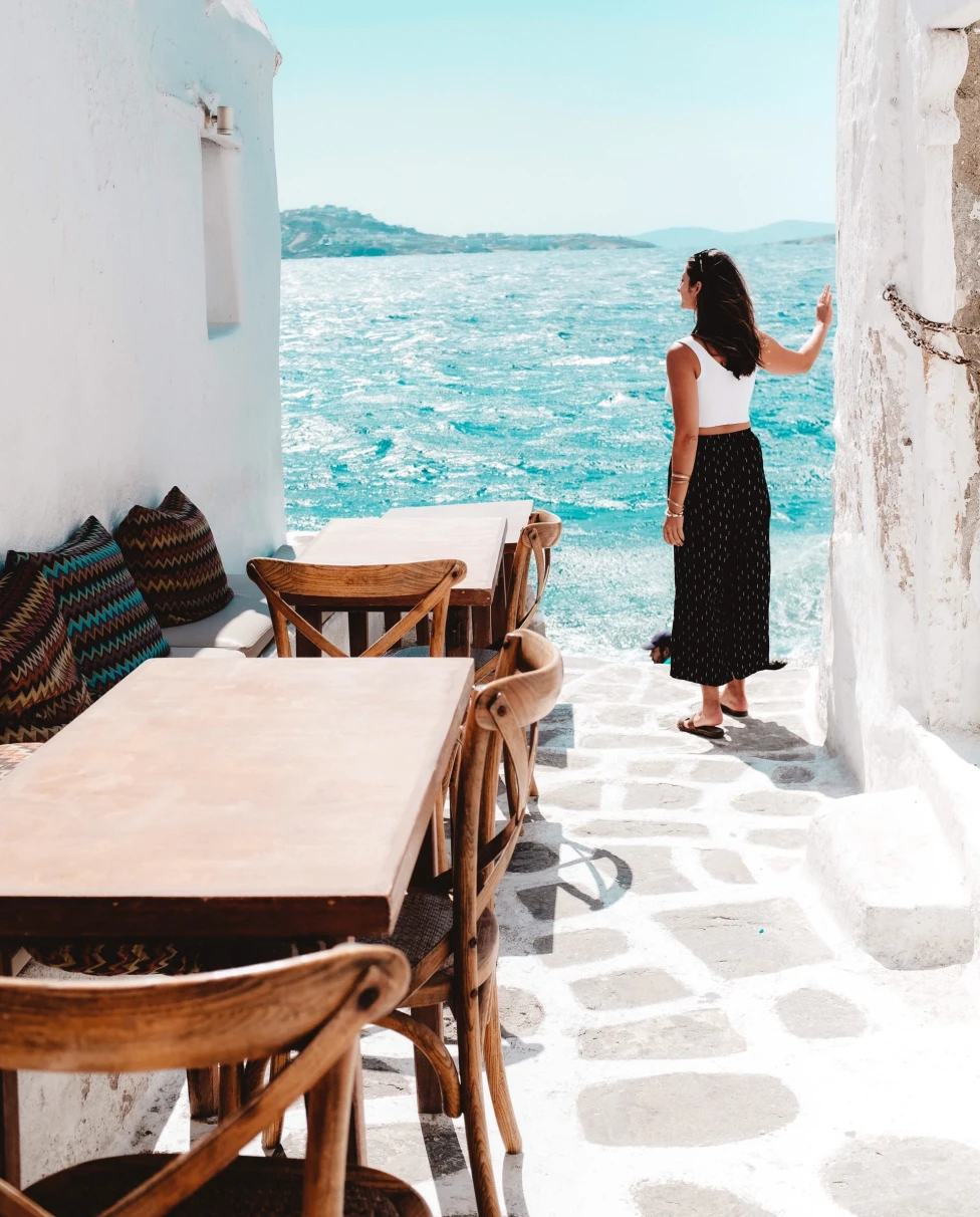 Woman wearing black skirt and white shirt standing next to white building and body of water during daytime