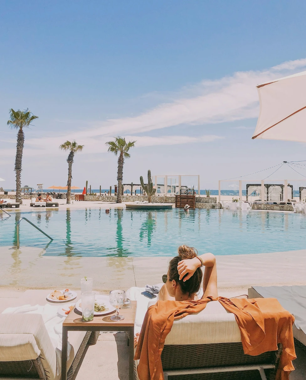 A woman lying on a lounge chair next to a pool area during the daytime