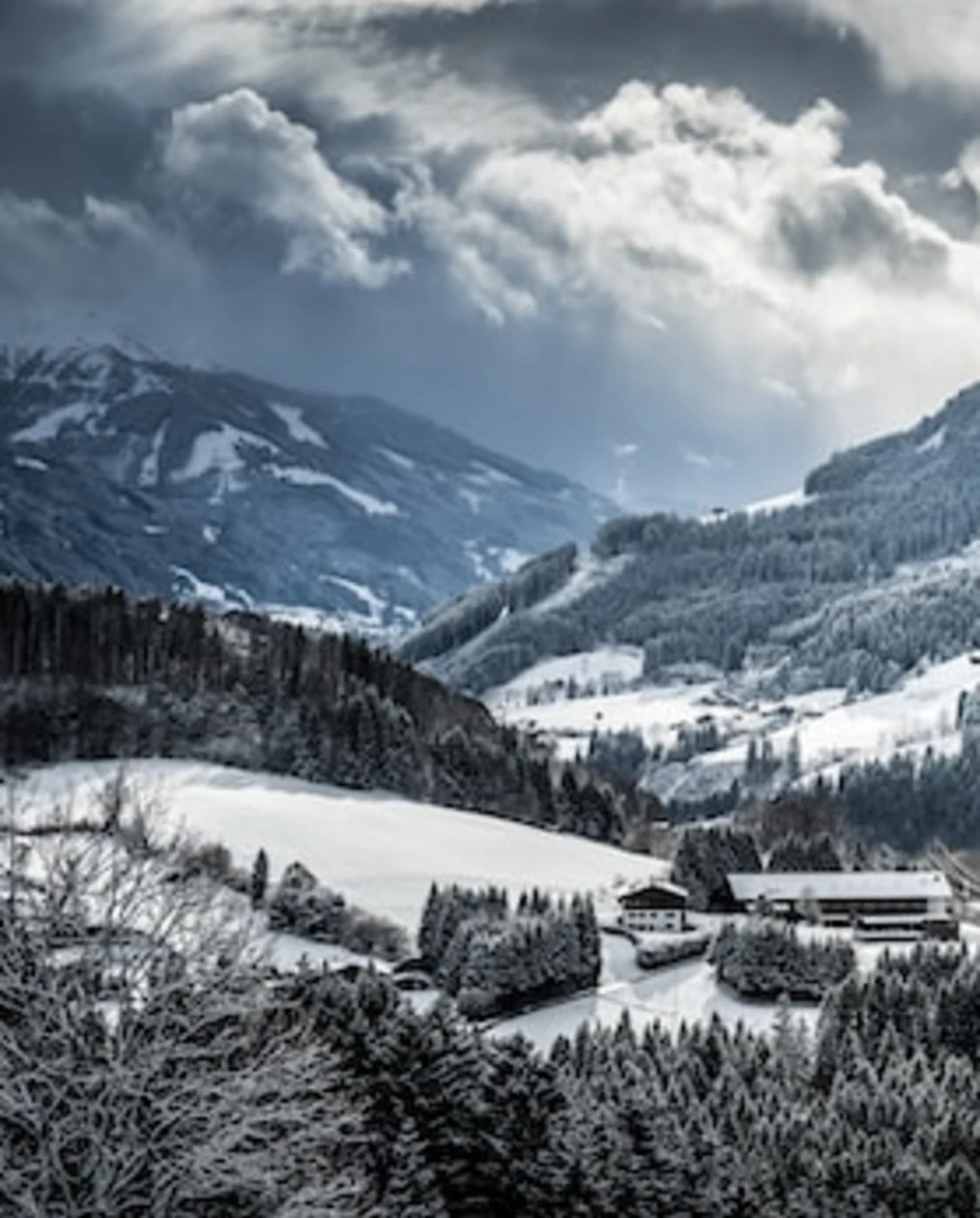 A building in the middle of a snowy valley with tall mountains and trees on either side