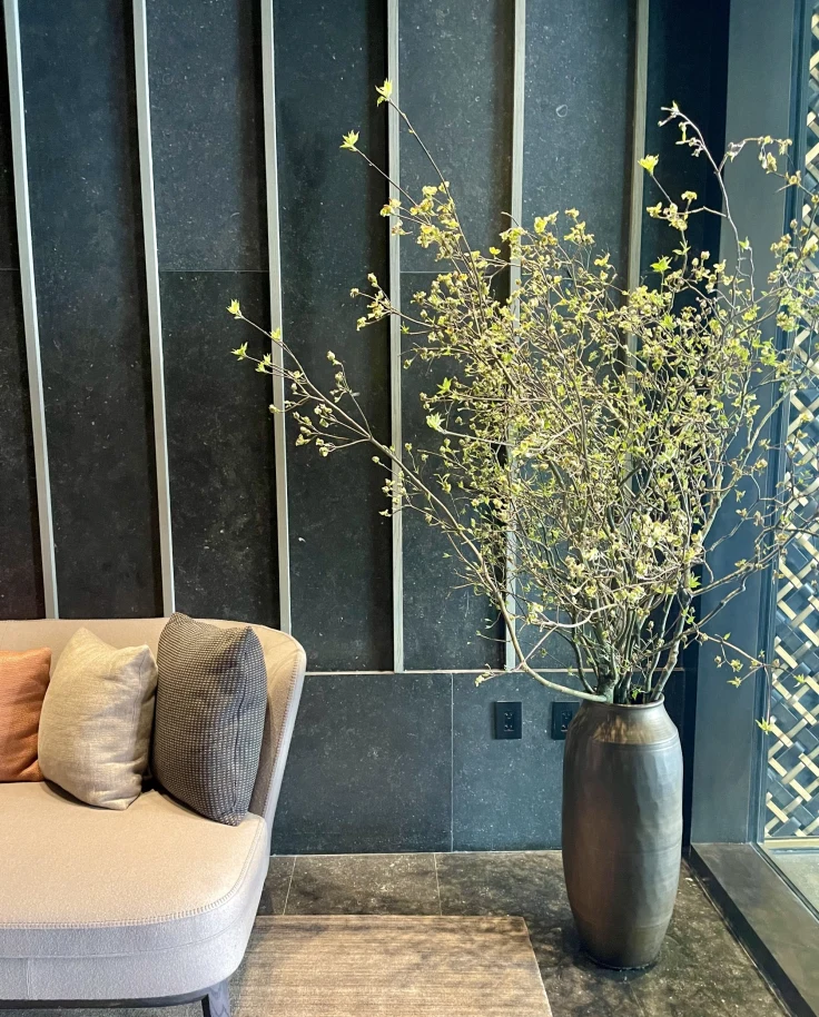Inside the hotel, showcasing room details, such as a couch with pillows and a plant in a silver vase.