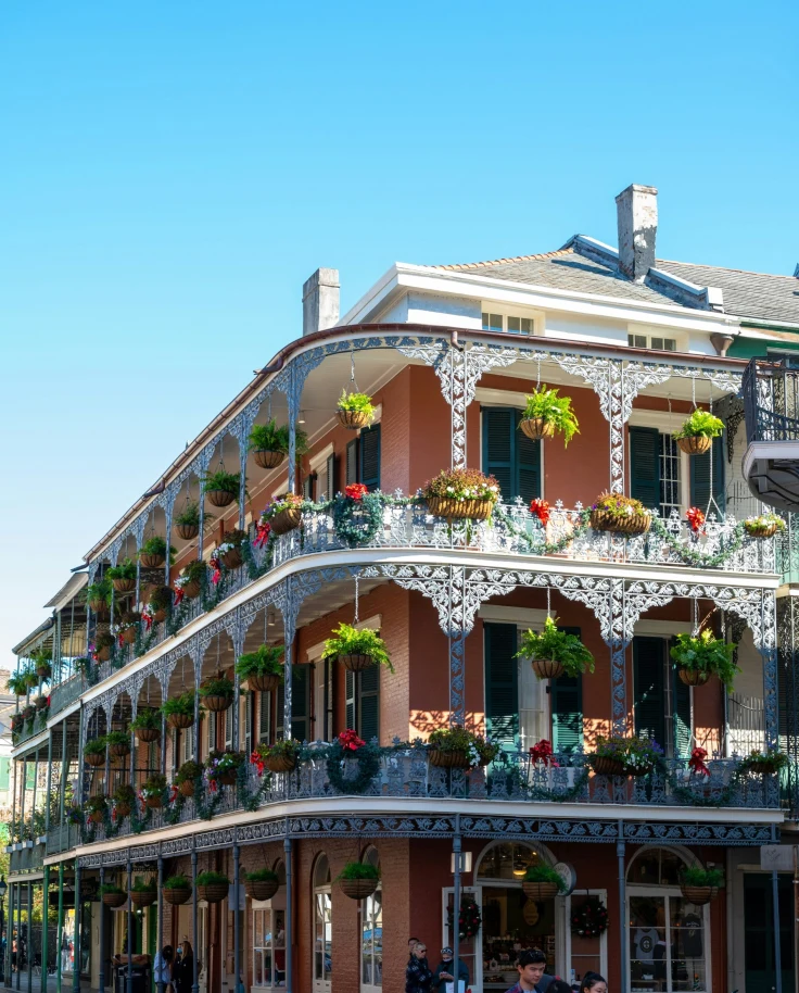 The corner of a three-story building in New Orleans with balconies and hanging plants.