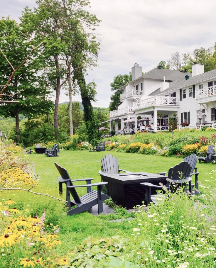 The hotel and its sprawling grounds with lush foliage and a patio table and chairs set in the garden.