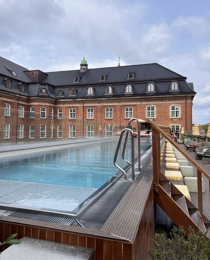 An outside swimming pool during the daytime with a red brick building in the background