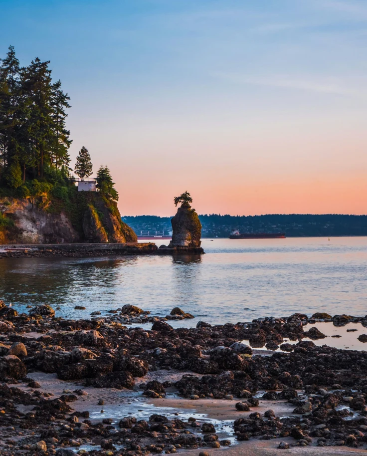 View of rocks rising out of the water near a shore at dusk.