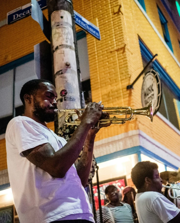 A group of people playing brass instruments in a crowd outdoors on Royal Street, New Orleans with a yellow colored building behind