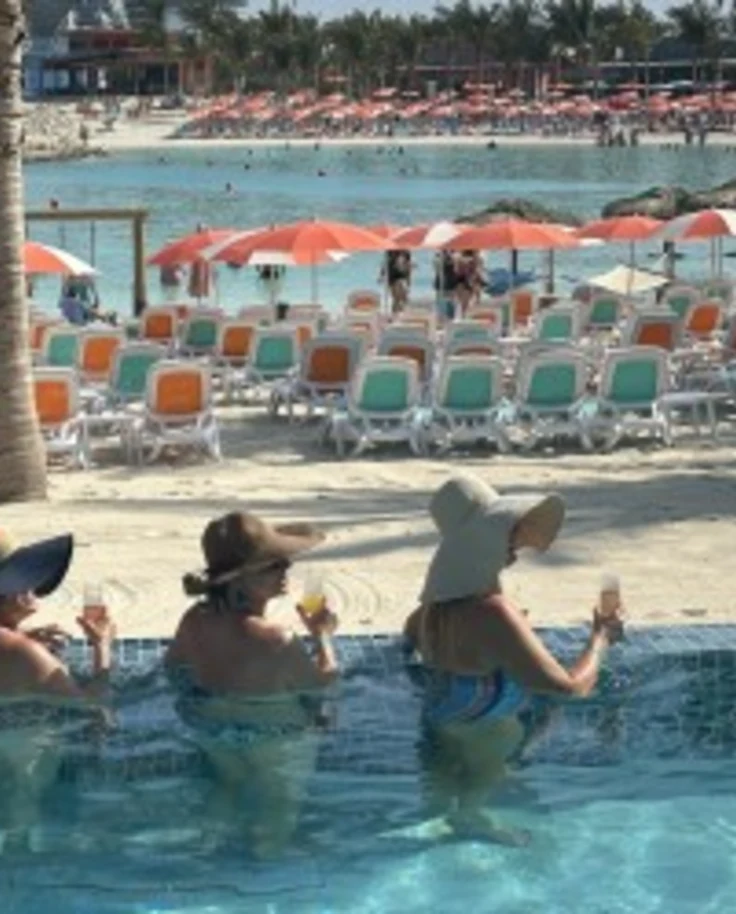 Four friends in the pool near the beach with drinks in hand.
