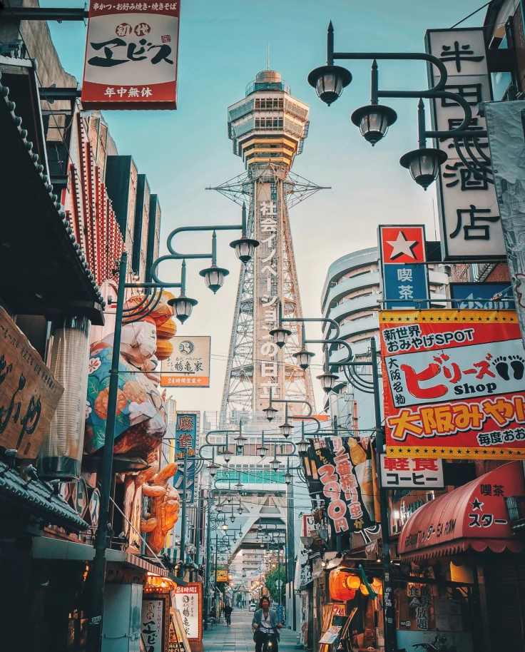 A low-angled view of a city street with colorful billboards and a tower in the distance