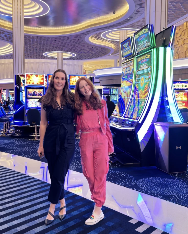 A woman in a black jumpsuit and a woman in a pink jumpsuit standing on a casino floor.