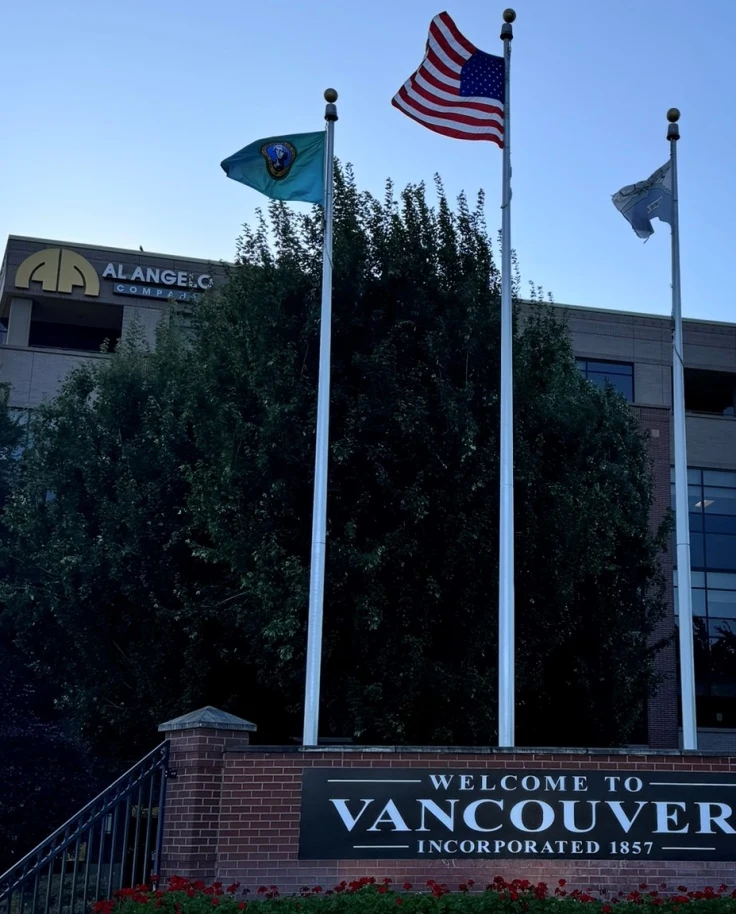 A sign that says "Welcome to Vancouver" with three flags and a building in the background.