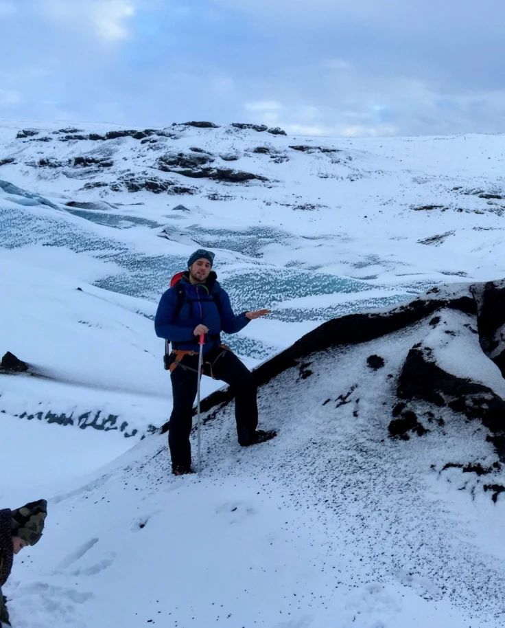 A person posing on a snowy hill surrounded by rocky and snowy terrain.