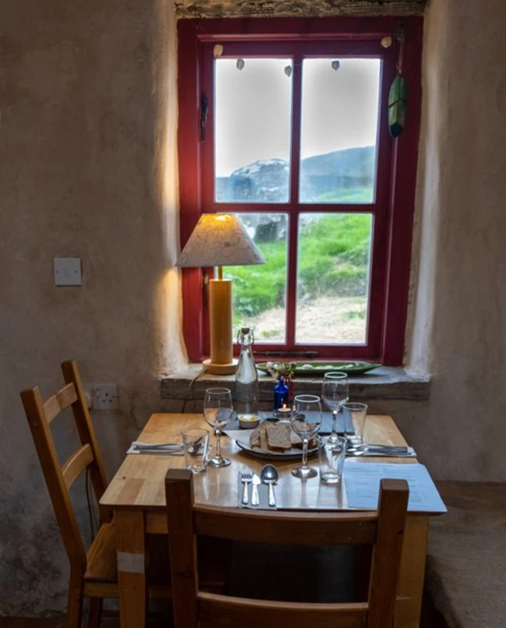 The interior of a restaurant with a table and two chairs and a large window looking out to the Irish countryside