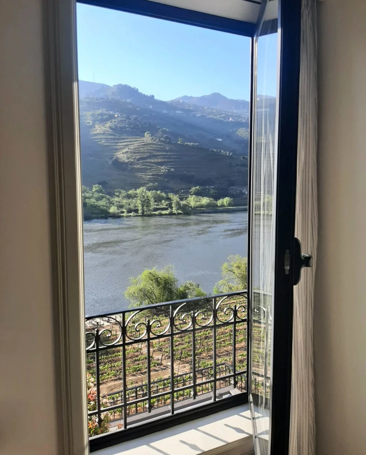 A view of a lake and mountains on a sunny day from inside a hotel room, through an open door.