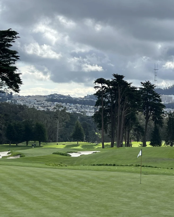 A view of a hole on a golf course with a city view in the background.