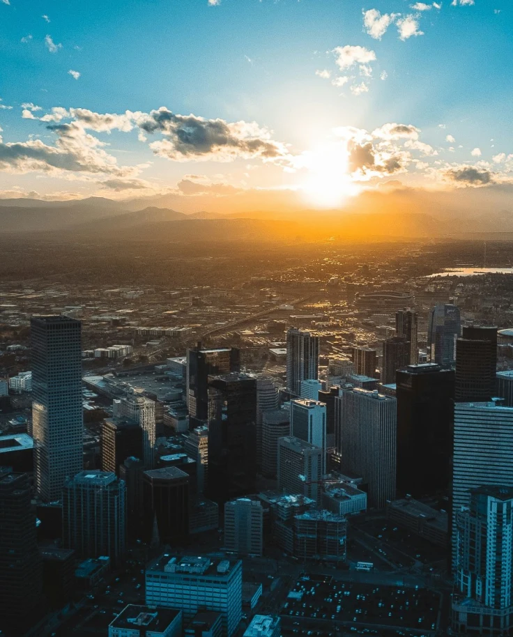 A bird's eye view of the city of Denver as the sun sets over the mountains with clouds reaching toward the horizon.
