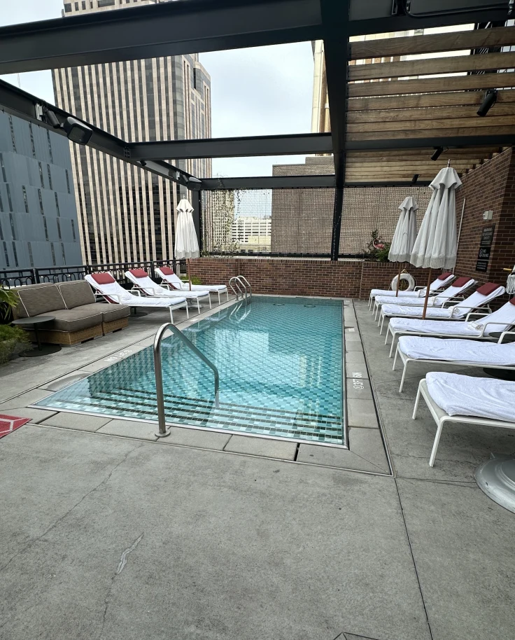 The rooftop pool at Virgin Hotels New Orleans with white sun loungers and umbrellas and a concrete floor and dark beams overhead