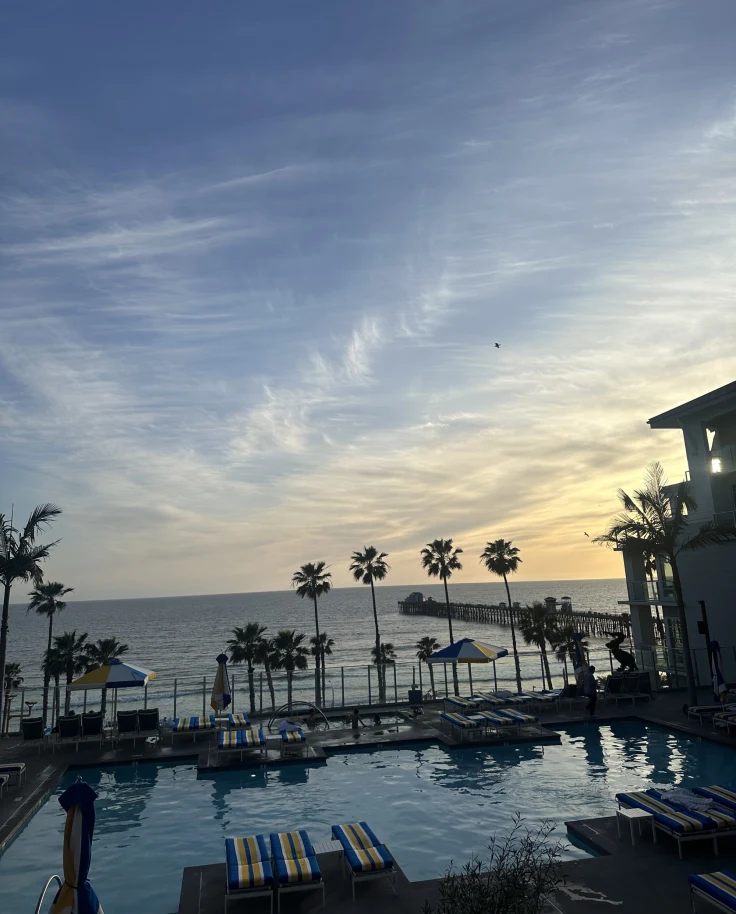 A view of a hotel pool next to the ocean during a sunset