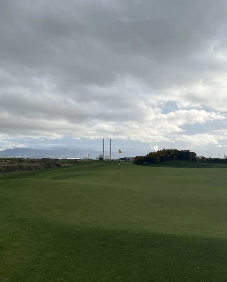 A green golf course and sand pit of a golf course on a cloudy day.