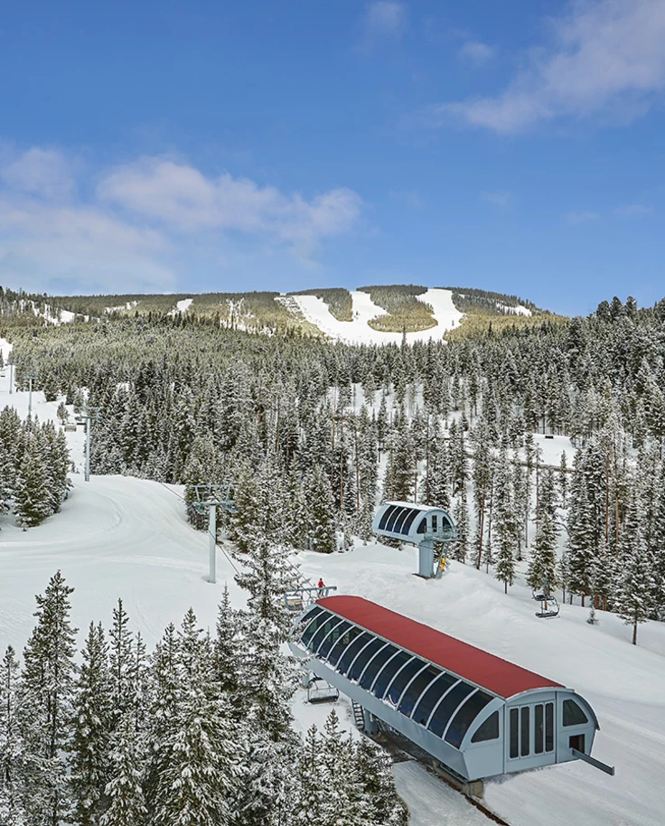 An aerial view of a ski resort with snowy hills, a mass amount of pine trees and ski lifts.