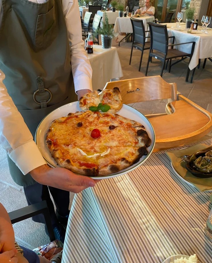 A person holding a pizza decorated with a face at Castelfalfi, Tuscany.