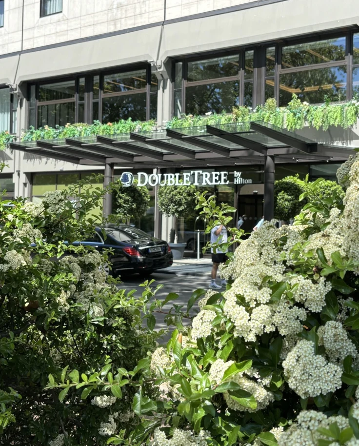 The exterior of the DoubleTree as seen through a hedge with white flowers.