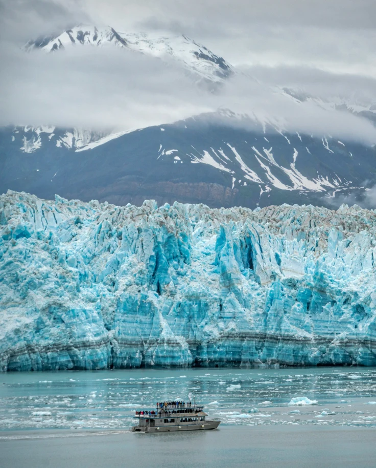 White ship on a body of water sailing past glaciers on a cloudy day.