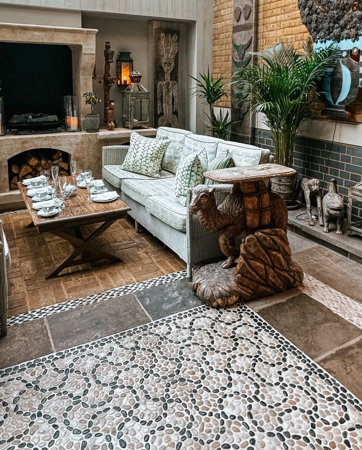 A beautiful hotel lobby with mosaic tile flooring, a white sofa, coffee and side tables, windows, glass ceilings and decorative plants near various pieces of art.