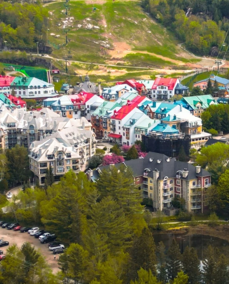 View overlooking a ski village in the summertime with green slopes and red and green buildings among the trees.