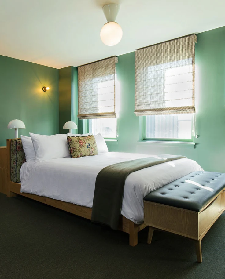 A large green bedroom with a leather couch and a wooden bed in the center of the room.