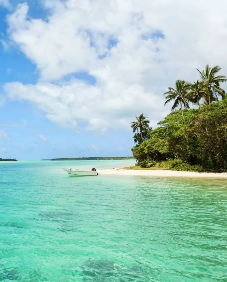 A view of the clear, azure sea, with a small boat, and shores full of natural greenery.