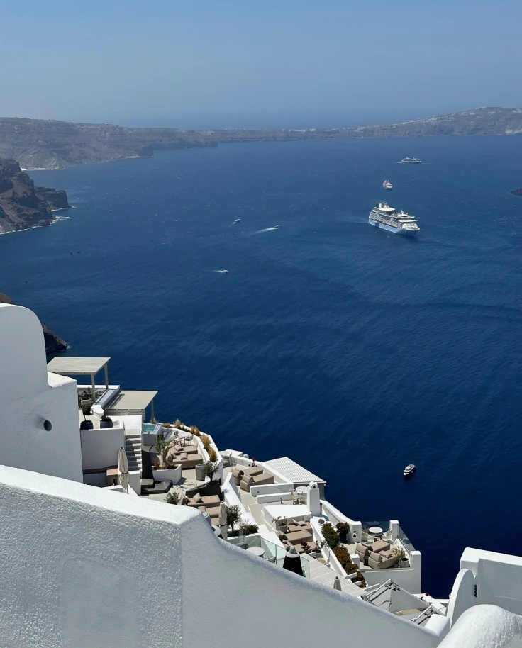 A boat in the ocean off the coast of Santorini with white buildings. - Kristyne Wada