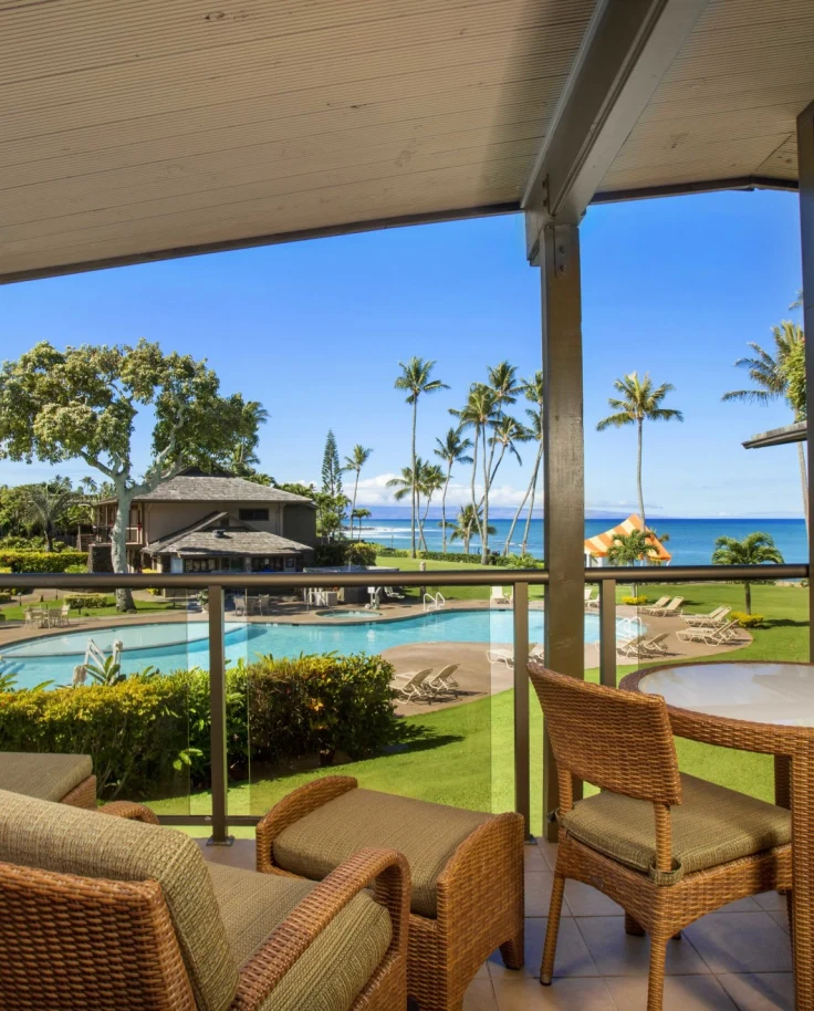 A hotel patio with furniture looking out on a green lawn and palm trees