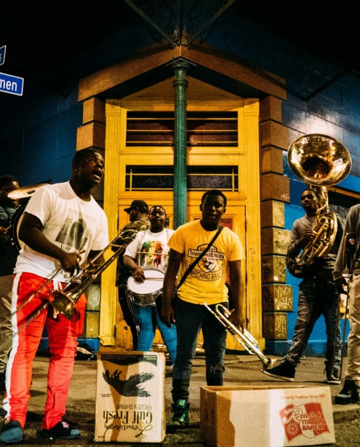 A group of people playing instruments outside in front of a yellow and blue building at nighttime.
